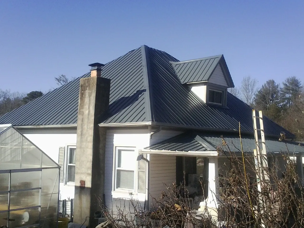 Dark blue standing seam metal roof on a white farmhouse with dormer — Slate & Tile Roof Repair by Roofing Brothers in Eddyville