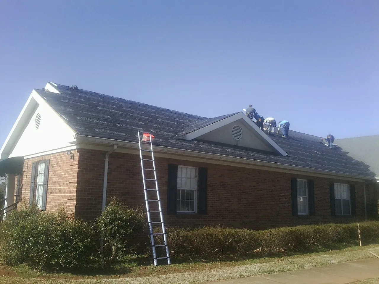 Crew tearing shingles off a brick ranch roof with a ladder set — Metal Roof Repair work by our crew in Eddyville