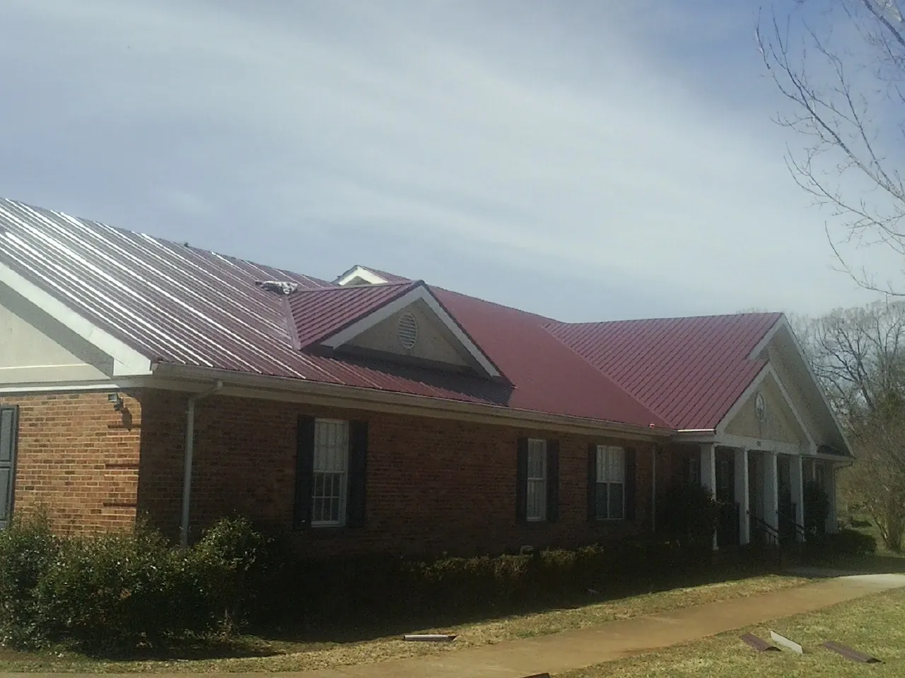 Red metal roof with gabled entries on a long brick building, from a Hail Damage Roof Repair job in Eddyville