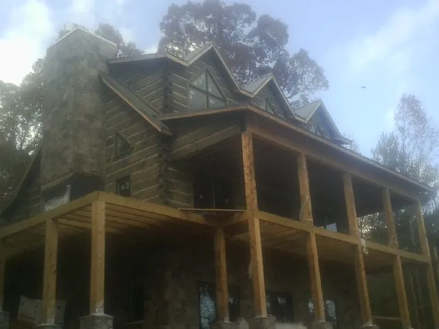 Stone chimney and dormers on a large log home with a timber porch in Eddyville