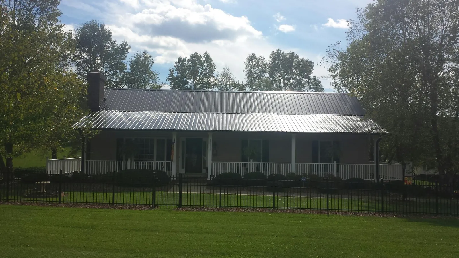 Gray metal roof on a brick ranch with a full width front porch — Gutter Guard Installation work by our crew in Eddyville