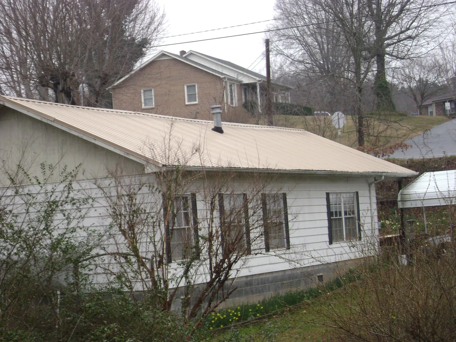 Tan metal roof on a white sided house set into a hillside — Commercial Roofing by Roofing Brothers in Eddyville